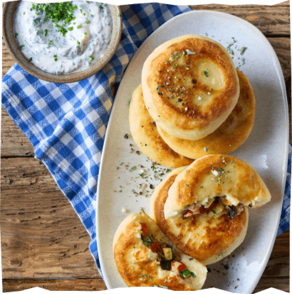 Gefüllte Kartoffelküchlein mit würziger Füllung und Dip auf einem blaukarierten Stofftuch.