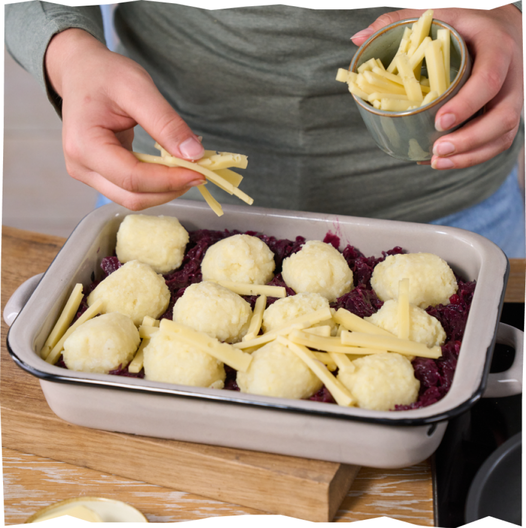 Über den Rotokohl-Kloß-Auflauf werden Raclette-Käse-Scheibchen gestreut.