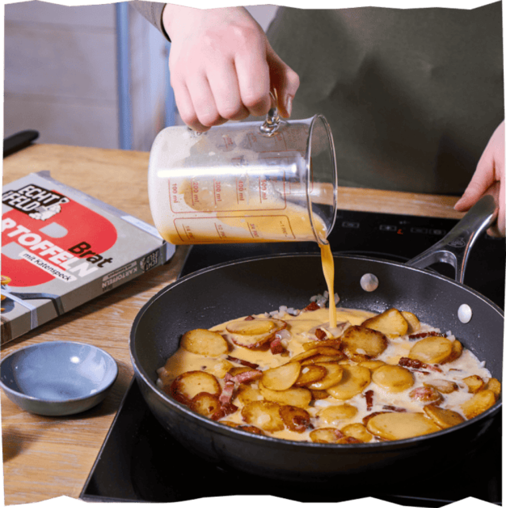 Hinzufügen der Eiermasse zu den angebratenen Bratkartoffeln für das perfekte Bauernfrühstück.
