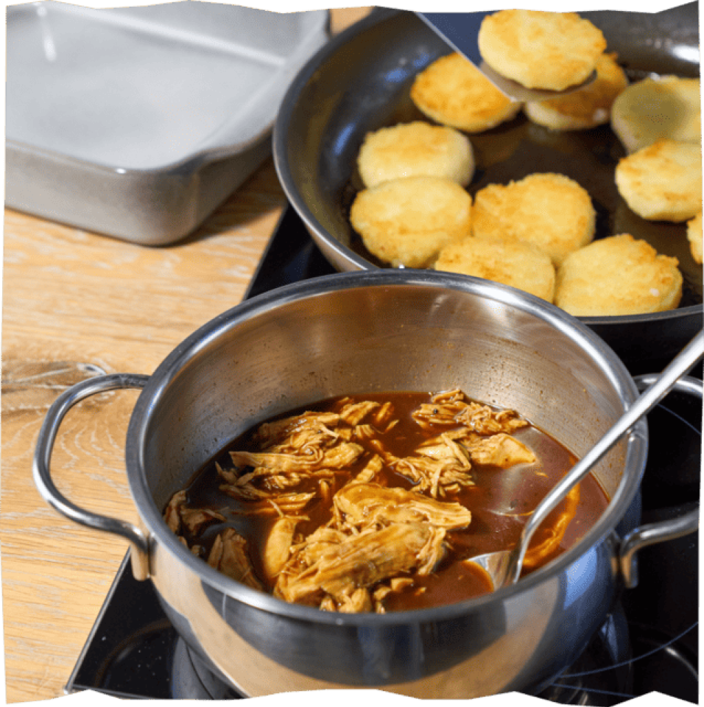 Pulled Chicken und angebratene Kartoffelkloßscheiben auf zwei Herdplatten.