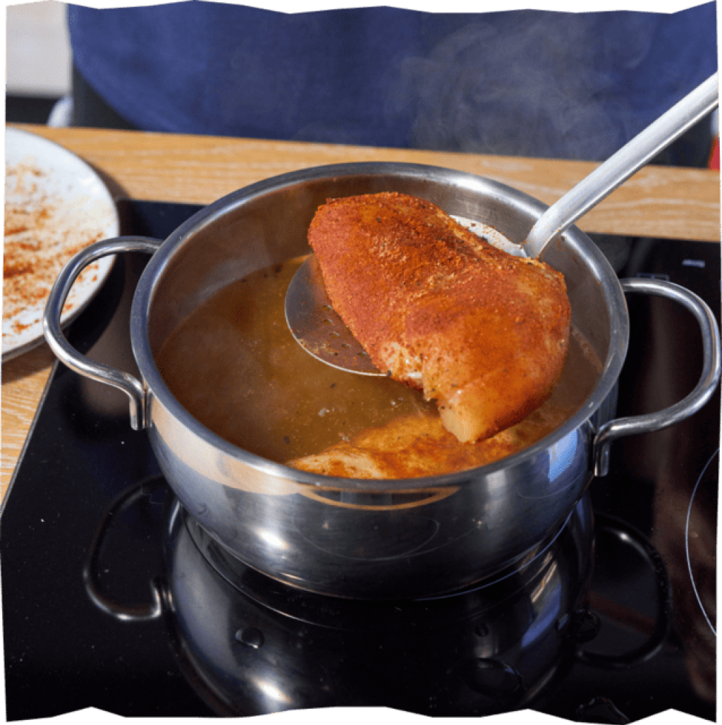 Gewürztes Hähnchenbrustfilet, das für das Pulled Chicken in heiße Hühnerbrühe gelegt wird.