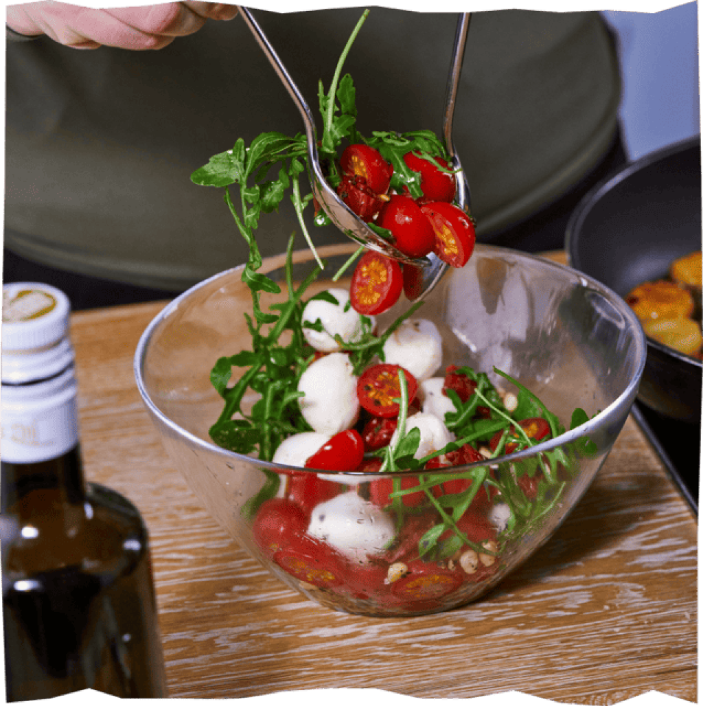 Mozzarella, Cocktailtomaten und Rauke, die mit dem Dressing für den Gnocchi-Salat vermengt werden.