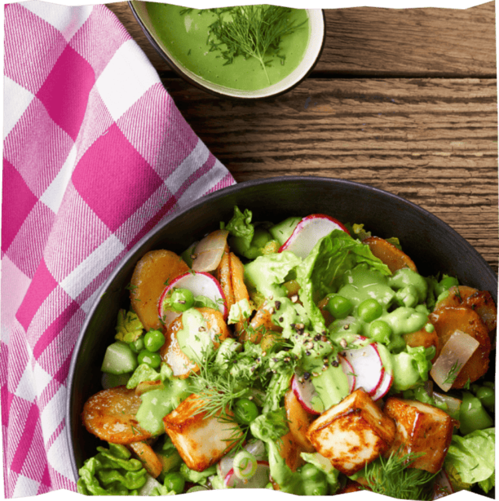 Green Goddess Salat mit Bratkartoffeln und Halloumi auf einem Holztisch.