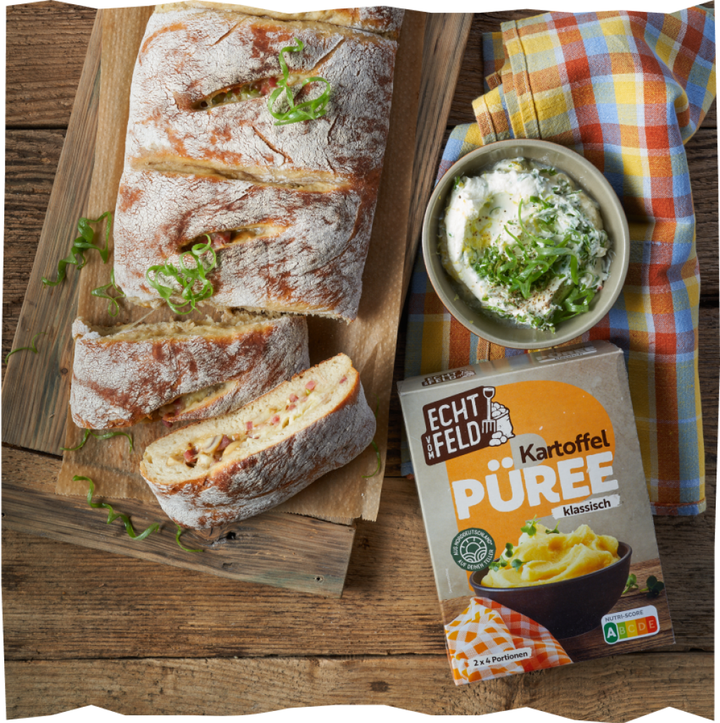 Handbrot mit Speck-Champignon-Käse-Füllung mit einem Schmand-Zitronen-Dip auf einem Holzbrett und einer karierten Serviette angerichtet.