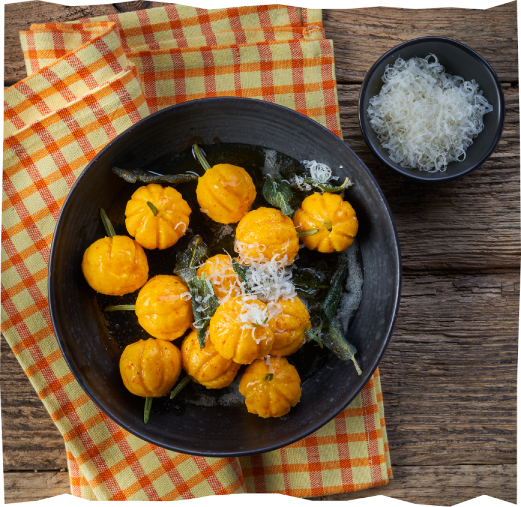 Kürbis-Gnocchi mit Salbeiblättern und Parmesan auf einem orange-rot-karierten Tuch.