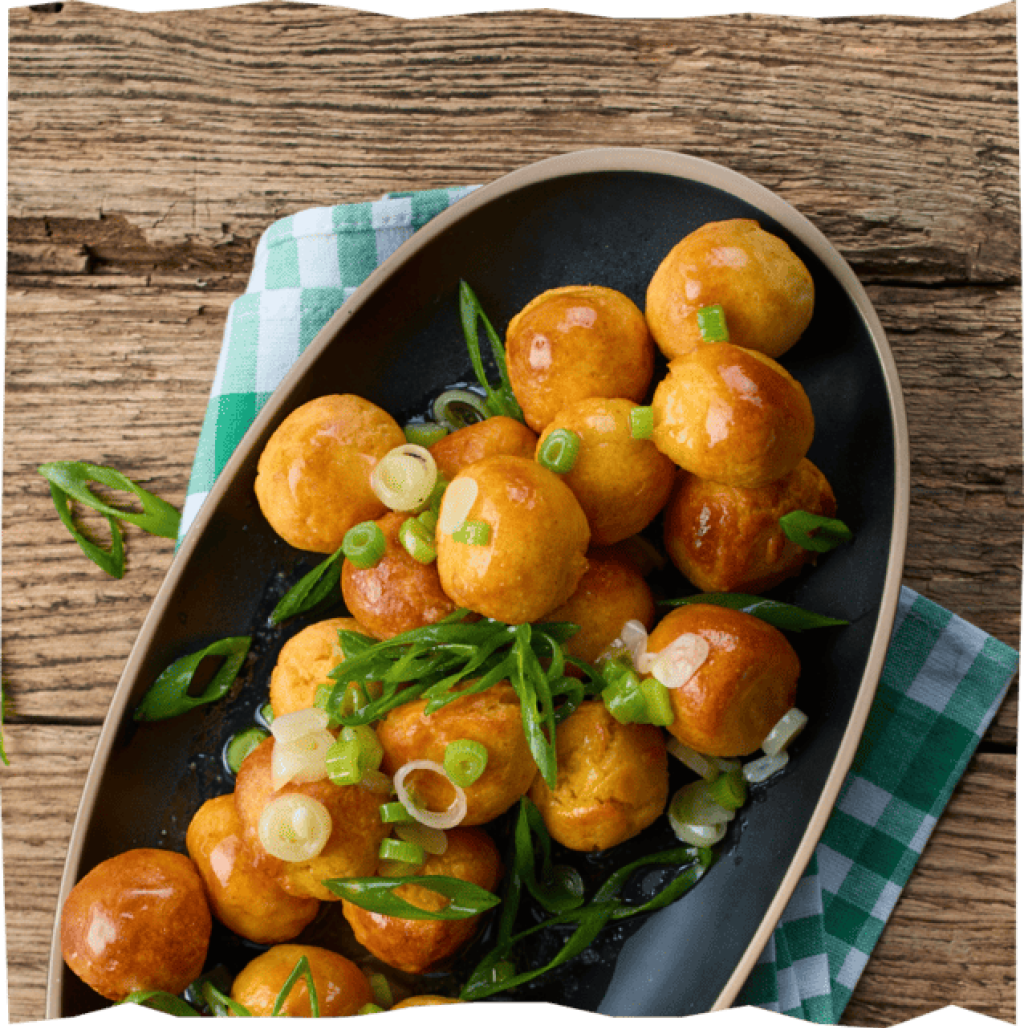 Goldbraune Kartoffelbällchen auf Servierplatte, bestreut mit frischen Lauchringen als Garnitur.