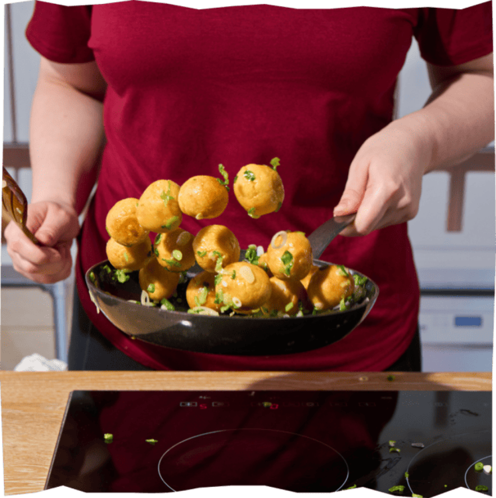 Kartoffelbällchen werden in einer Pfanne in Knoblauchbutter und Lauchzwiebeln geschwenkt.