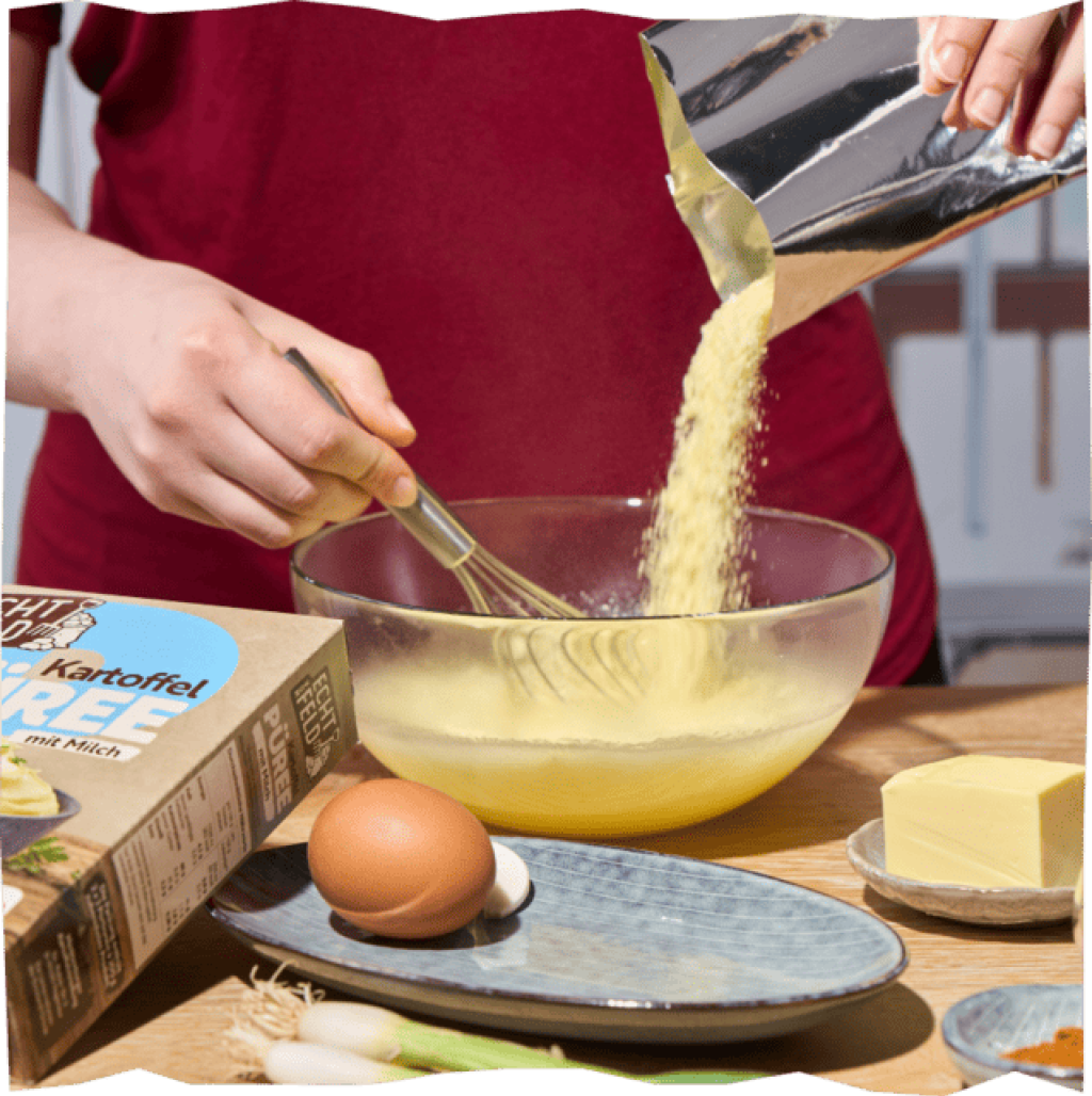 Kartoffelpüree-Pulver wird mit einem Schneebesen in eine Glasschale gerührt. Butter, Ei und Lauch daneben.