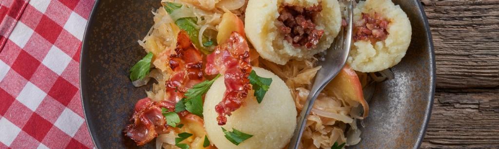 Kartoffelklöße mit Speck-Zwiebel-Füllung und aromatischem Sauerkraut auf einem Teller serviert.