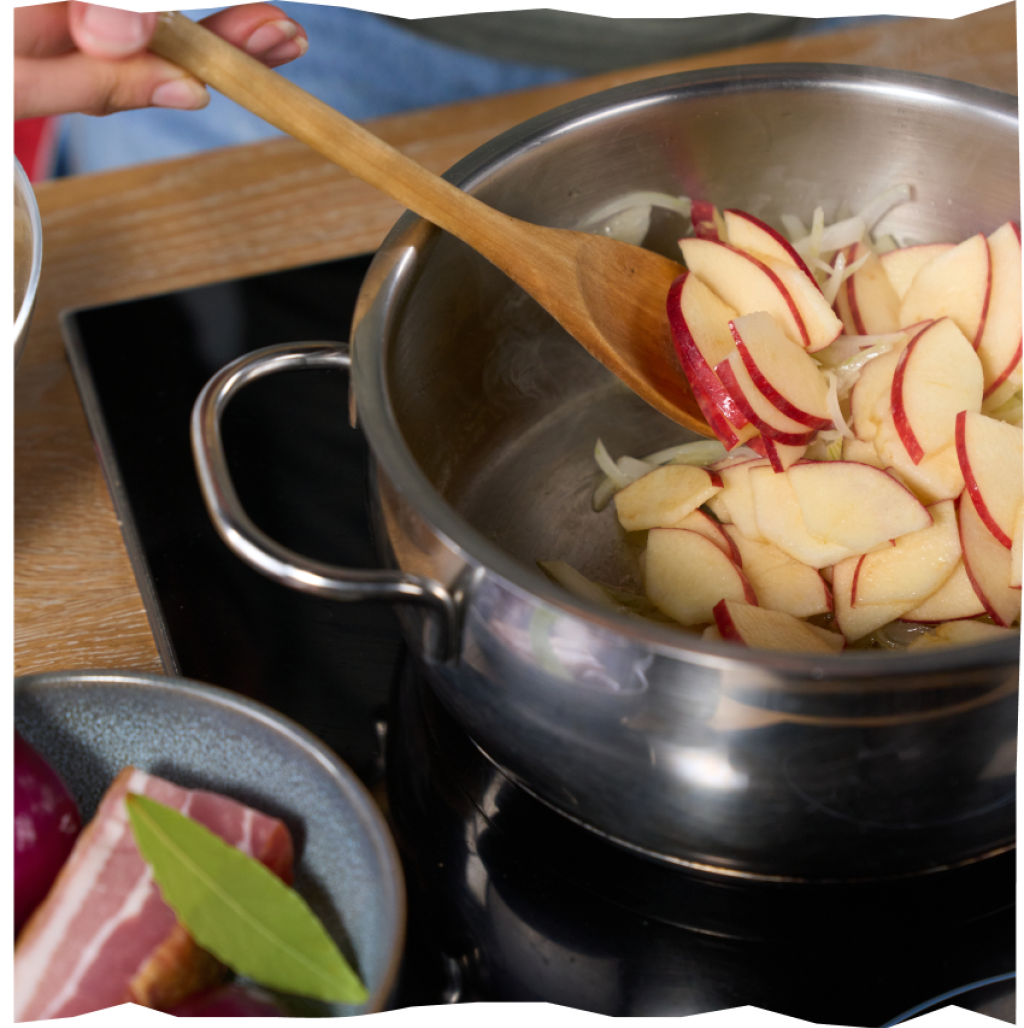 In Spalten geschnittene Äpfel und Zwiebel beim Anschwitzen in einem Kochtopf zur Vorbereitung des Sauerkrauts.