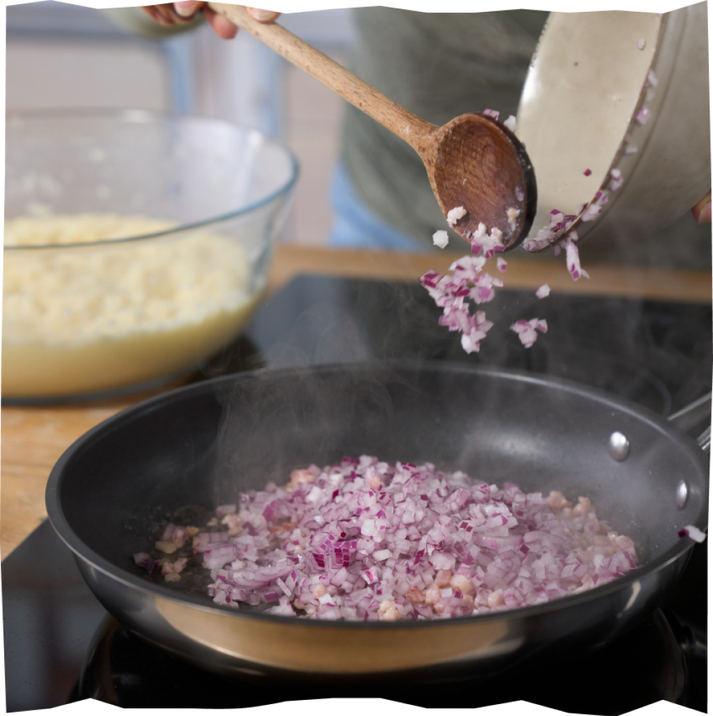 In feine Würfel geschnittene Zwiebeln und Speck beim Anbraten in einer Pfanne.