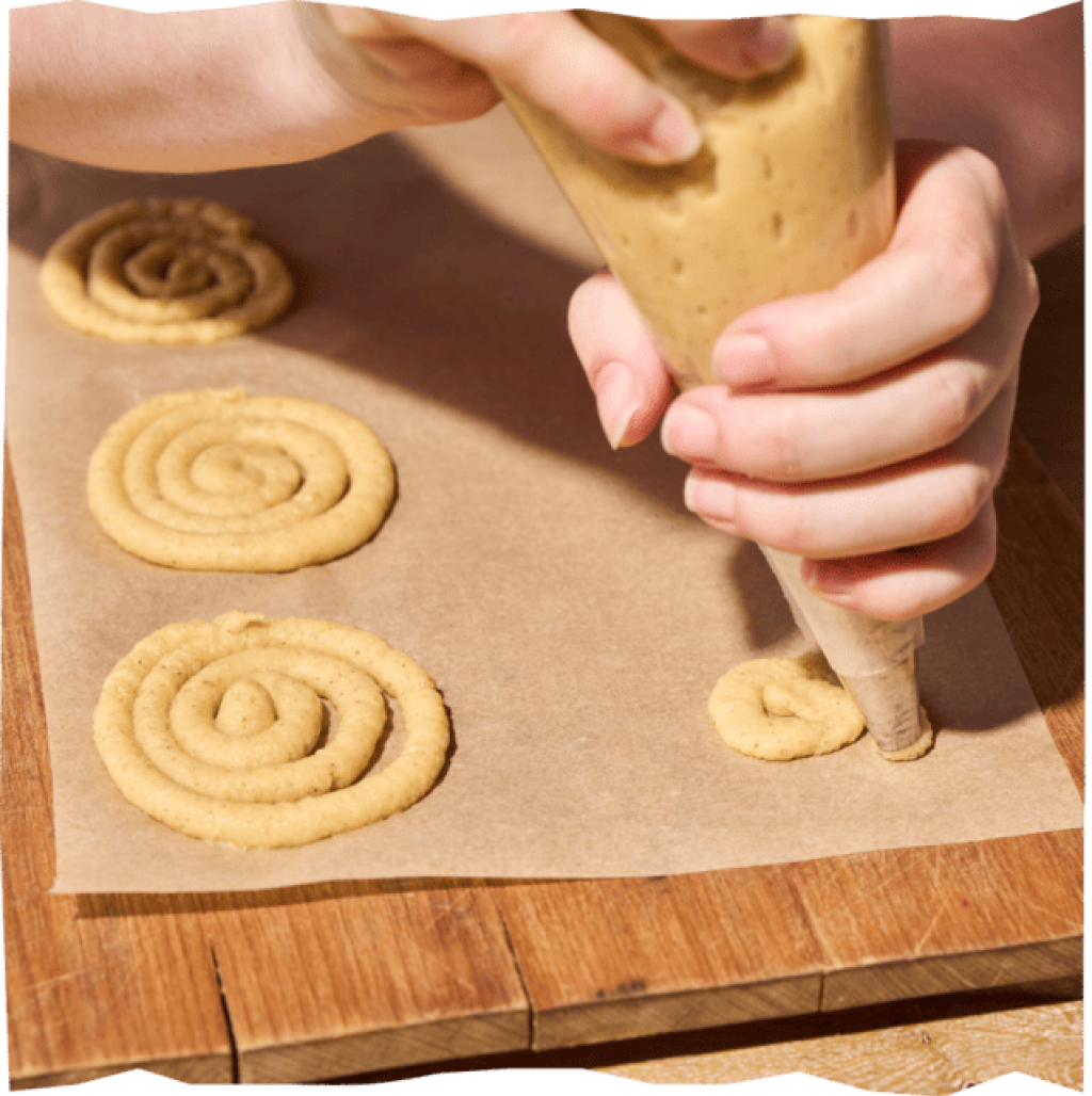 Die Kartoffelmasse wird mit einer Spritztüte als Swirls auf ein Backblech gespritzt.