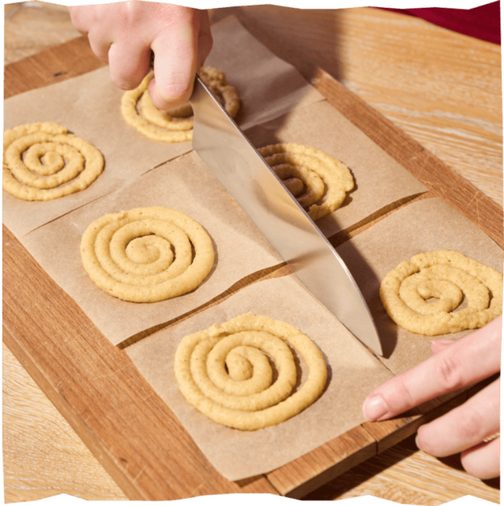 Backpapier wird mit einem Messer zugeschnitten. Auf den zugeschnittenen Rechtecken sind die Kartoffel-Swirls.