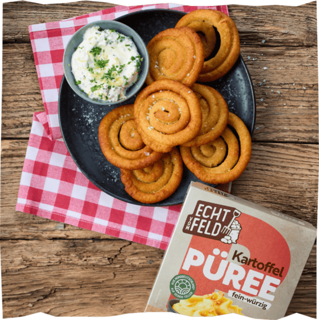 Goldbraune Kartoffel-Swirls auf dunklem Teller mit Kräuterdip, serviert auf rot-weiß karierter Tischdecke auf Holztisch.