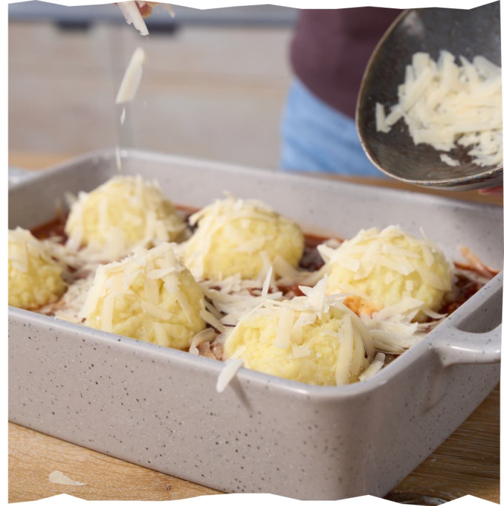Linsen-Bolognese und Kartofelklöße werden mit Parmesan bestreut, um im Ofen überbacken zu werden.
