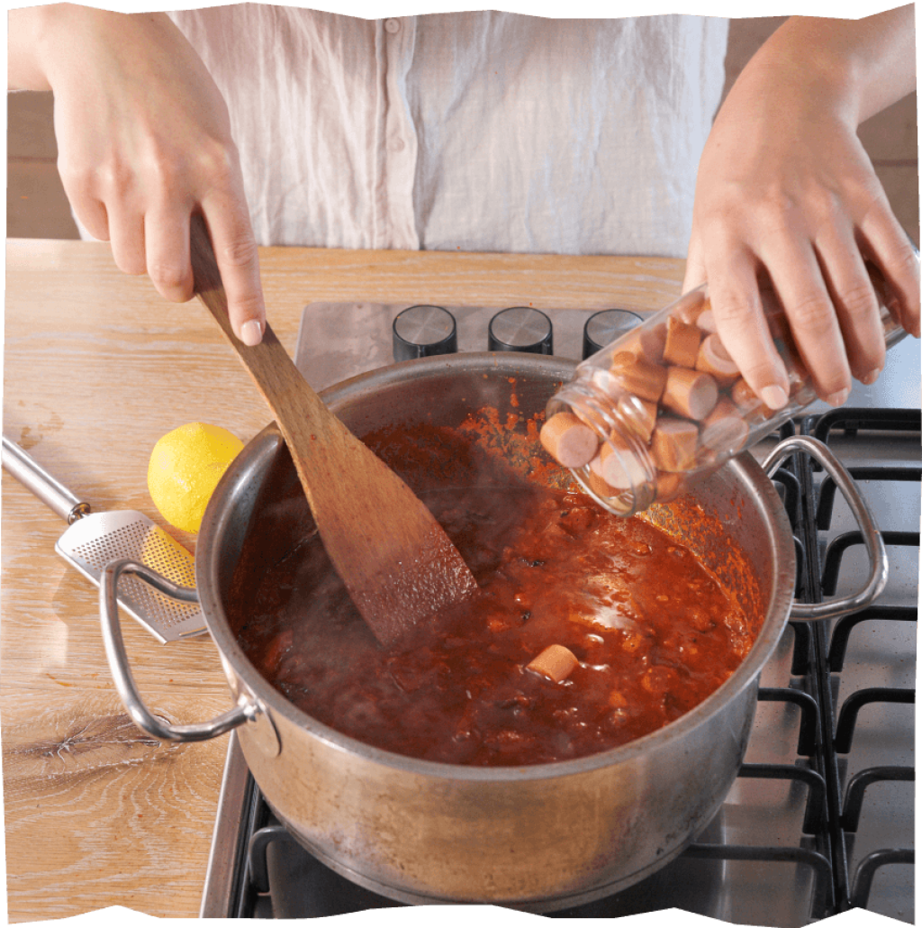 Hinzufügen von Wurststücken in den Tomatensud.