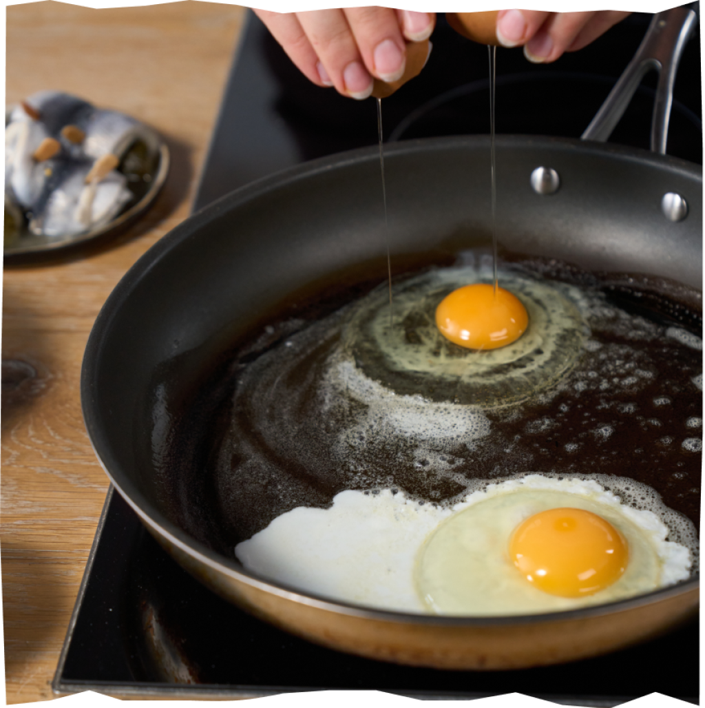 Zubereitung von zwei Spiegeleiern in einer mit Butter bestrichenen Pfanne.