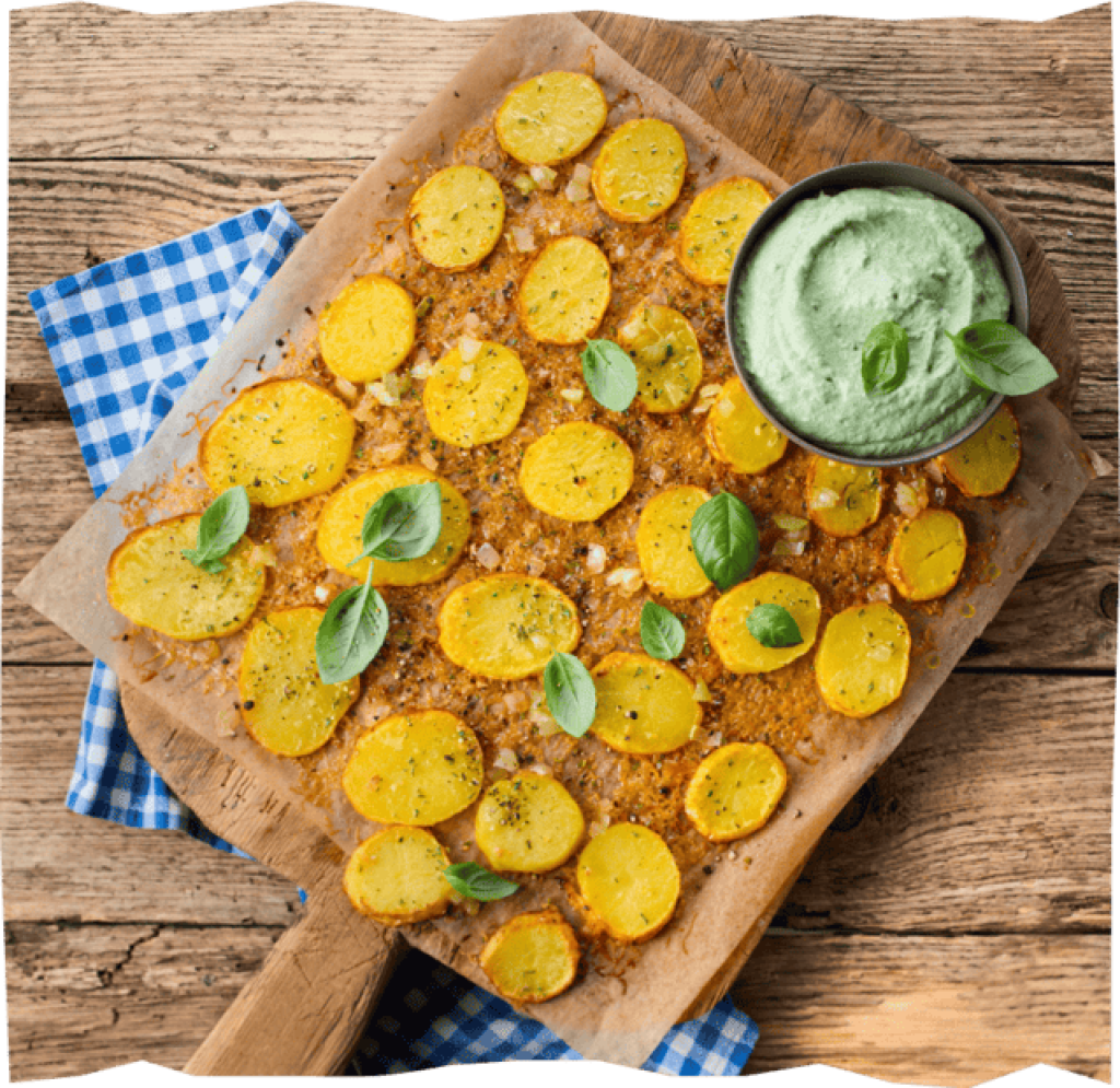 Goldbraune Bratkartoffeln auf einem Backblech mit Basilikum Blättern garniert, daneben ein Schälchen mit Kräuterdip.