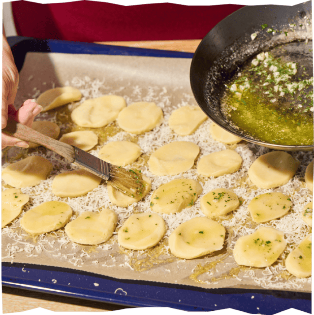 Kartoffelscheiben auf Backblech mit geriebenem Käse, bepinselt mit geschmolzener Kräuterbutter.