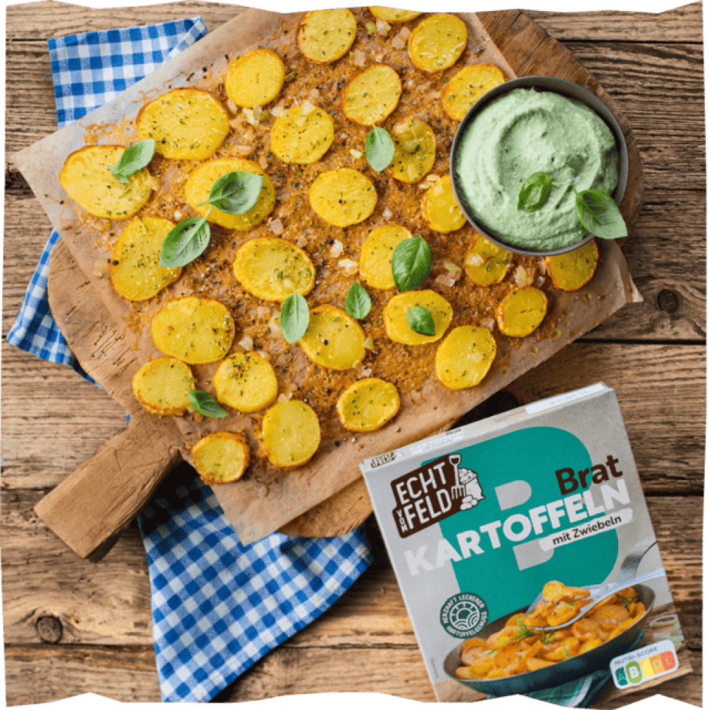 Goldbraune Kartoffelscheiben auf Holzbrett mit blau-weißem Tuch, daneben Packung Bratkartoffeln und Kräuterdip.