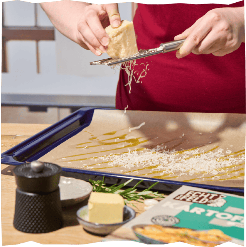 Der Käse wird mit einer Reibe über ein Backblech mit Backpapier gerieben.